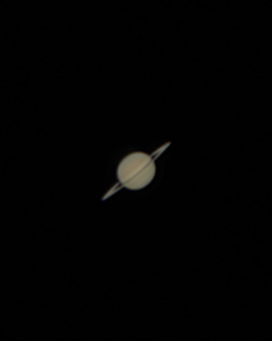 Saturn as a small pale disc with its rings tilted towards the camera.